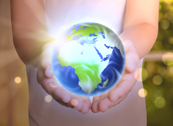 Woman holding Earth indoors, closeup. Bokeh effect