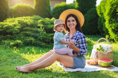 Photo of Mother with her baby daughter having picnic in garden on sunny day