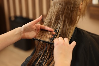 Professional hairdresser combing girl's hair in beauty salon, closeup