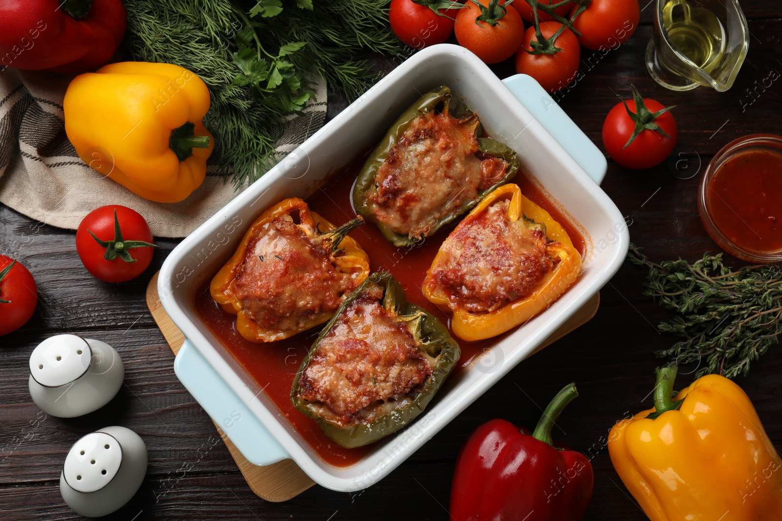 Photo of Tasty stuffed peppers in dish and ingredients on wooden table, flat lay