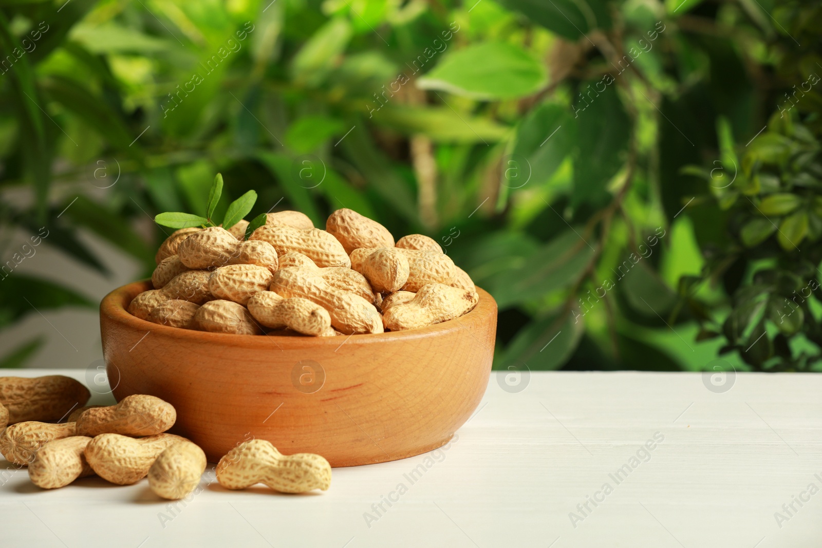 Photo of Fresh unpeeled peanuts in bowl on white table against blurred background, space for text