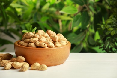 Photo of Fresh unpeeled peanuts in bowl on white table against blurred background, space for text