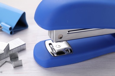 Photo of Blue stapler with staples on light wooden table, closeup
