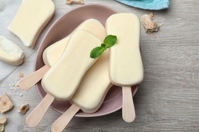 Delicious glazed ice cream bars, chocolate and mint on white wooden table, flat lay