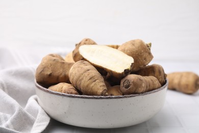 Photo of Whole and cut tubers of turnip rooted chervil in bowl on white tiled table, closeup