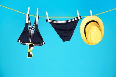 Photo of Beautiful bikini, hat and sunglasses hanging on rope against color background
