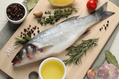 Tasty sea bass fish and spices on wooden table, flat lay