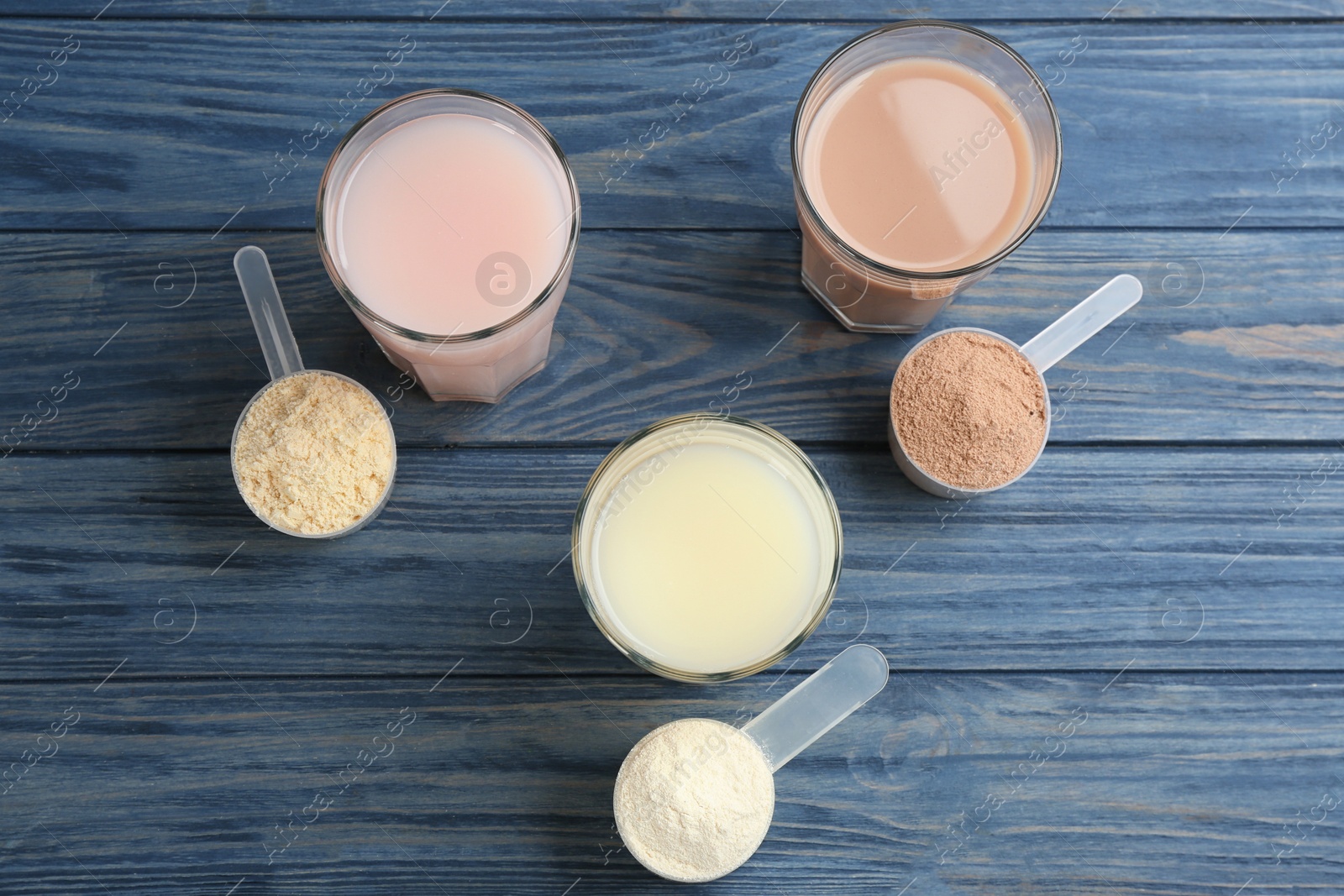 Photo of Protein shakes and powder on blue wooden table, flat lay