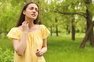 Young woman scratching neck outdoors, space for text. Seasonal allergy