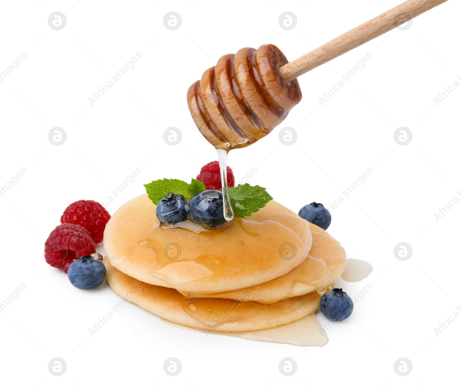 Photo of Pouring honey onto tasty pancakes with berries isolated on white
