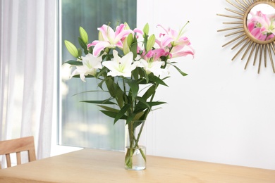 Vase with bouquet of beautiful lilies on wooden table indoors