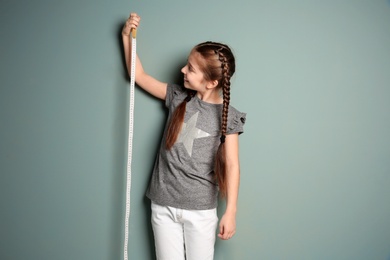 Little girl measuring her height on color background