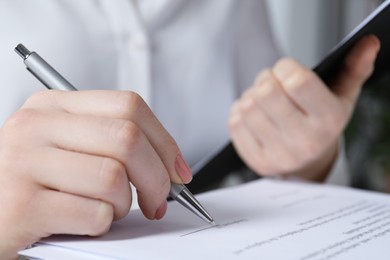 Woman signing document at table in office, closeup