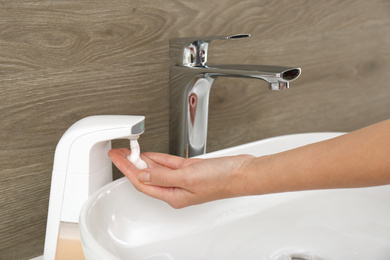 Woman using automatic soap dispenser in bathroom, closeup