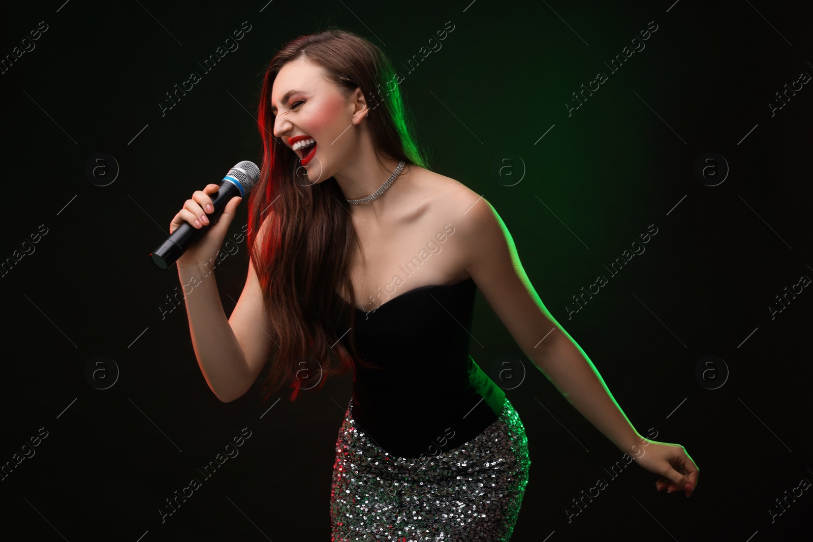 Photo of Emotional woman with microphone singing in color lights on dark background