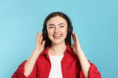 Happy woman in headphones enjoying music on light blue background
