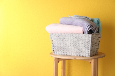 Photo of Basket with clean laundry on wooden table near yellow wall, space for text
