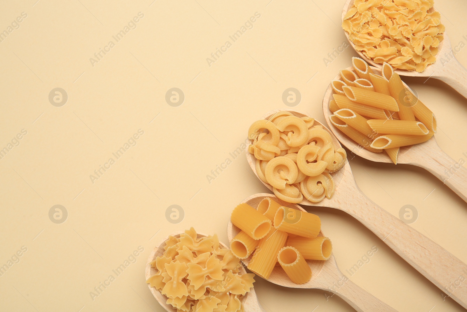 Photo of Different types of pasta in spoons on beige background, flat lay. Space for text