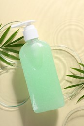 Bottle of face cleansing product, fresh leaves and petri dishes in water against beige background, flat lay