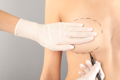 Photo of Doctor drawing marks on patient's breast for cosmetic surgery operation against gray background, closeup
