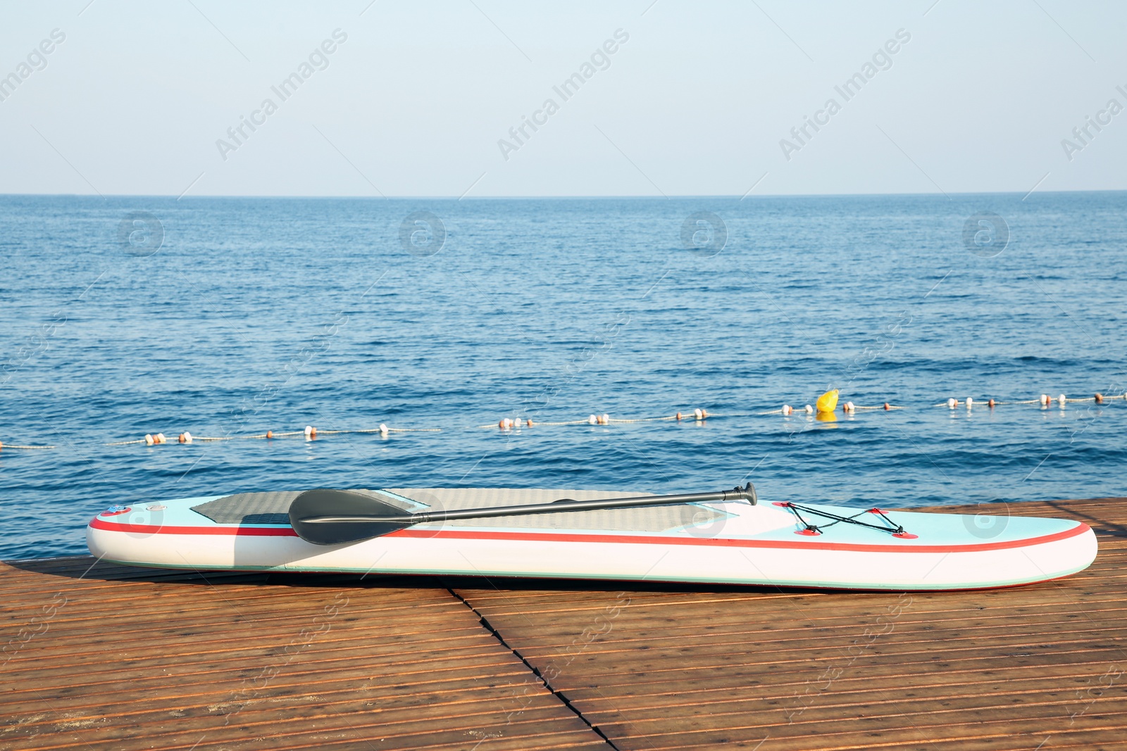 Photo of SUP board with paddle on wooden pier near sea