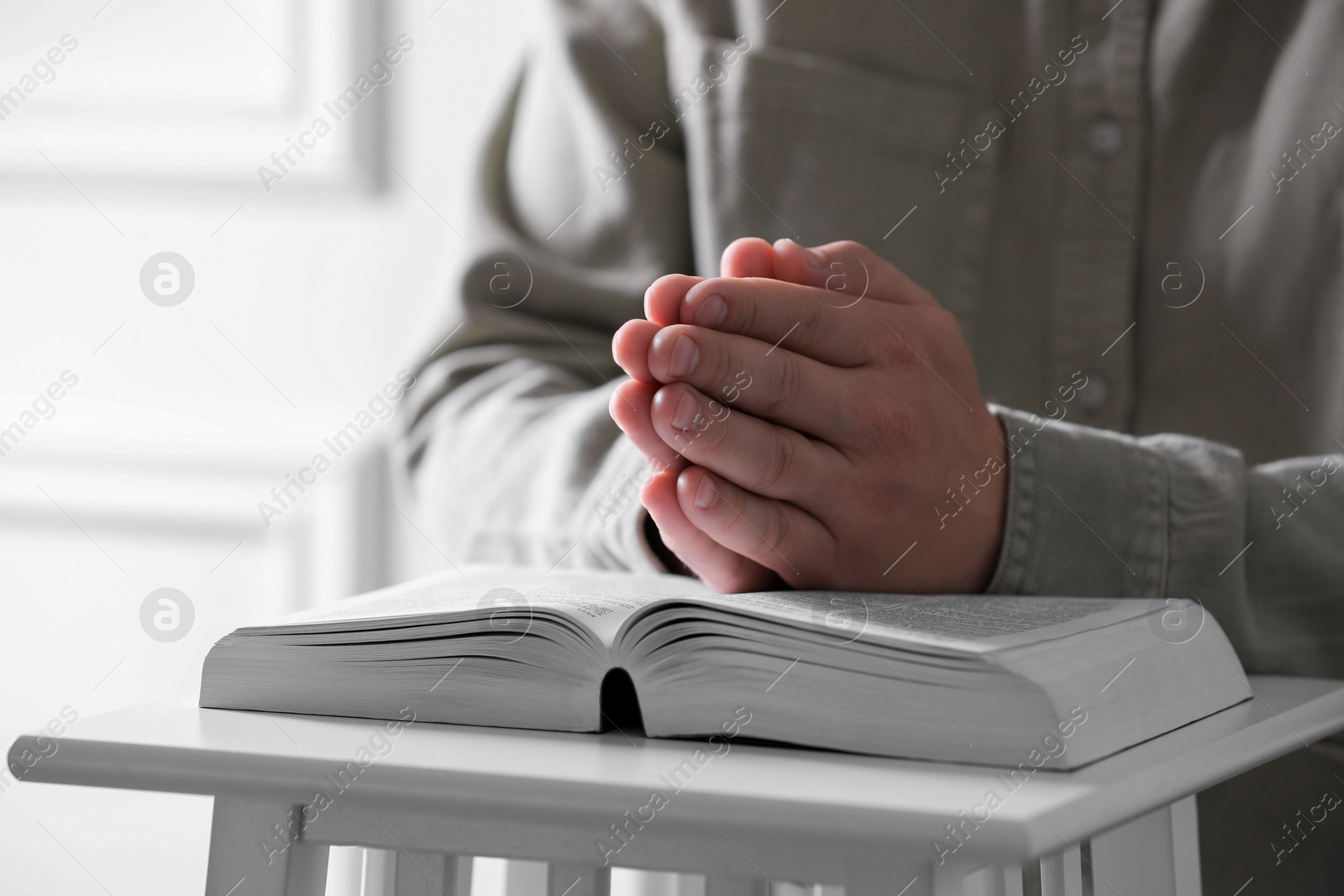 Photo of Religion. Christian man praying over Bible indoors, closeup