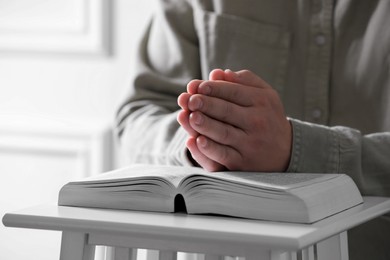 Religion. Christian man praying over Bible indoors, closeup