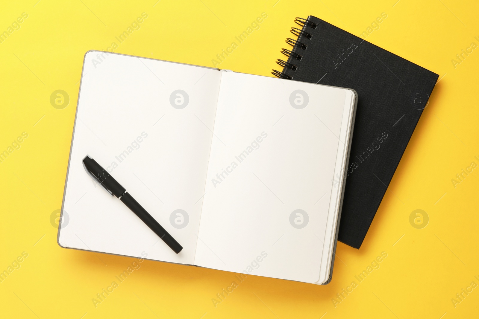 Photo of Notebooks and pen on yellow background, top view