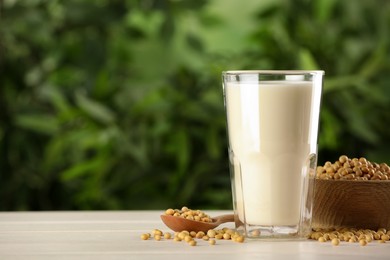 Photo of Glass with fresh soy milk and grains on white wooden table against blurred background. Space for text