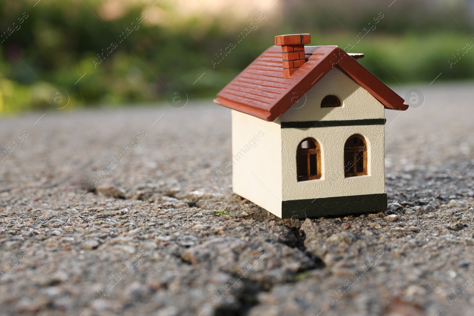 Photo of Wooden house model on cracked asphalt. Earthquake disaster