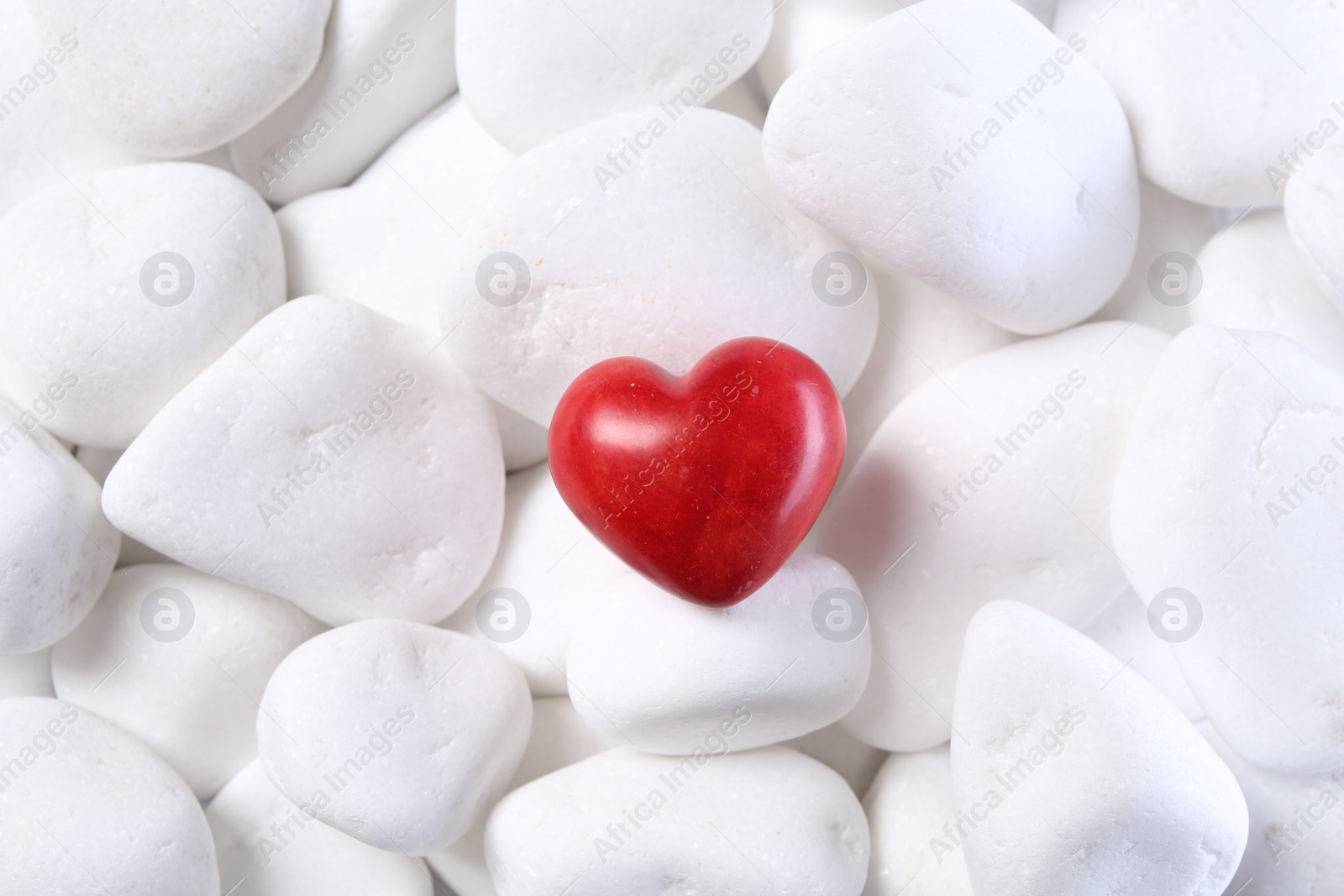 Photo of Decorative heart on white pebble stones, top view