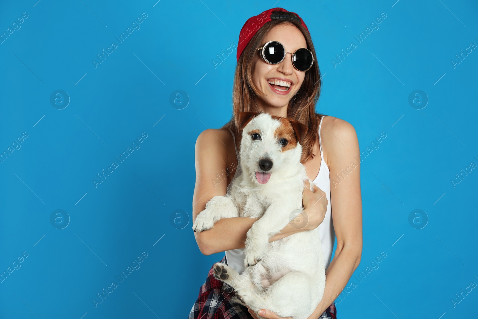 Photo of Young woman with her cute Jack Russell Terrier on light blue background. Lovely pet