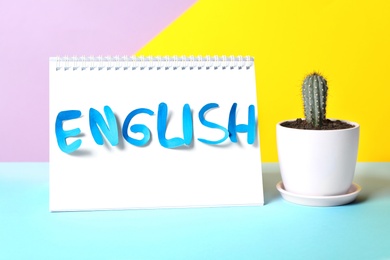 Photo of Notepad with word English and cactus on light blue table