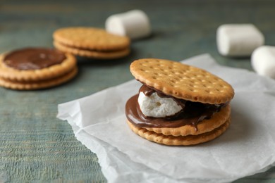 Photo of Delicious marshmallow sandwich with crackers and chocolate on light blue wooden table, closeup. Space for text