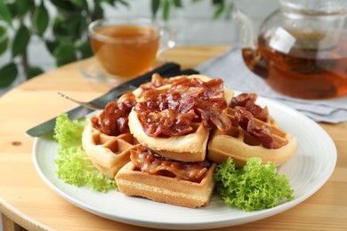 Tasty Belgian waffles served with bacon, lettuce and tea on wooden table, closeup