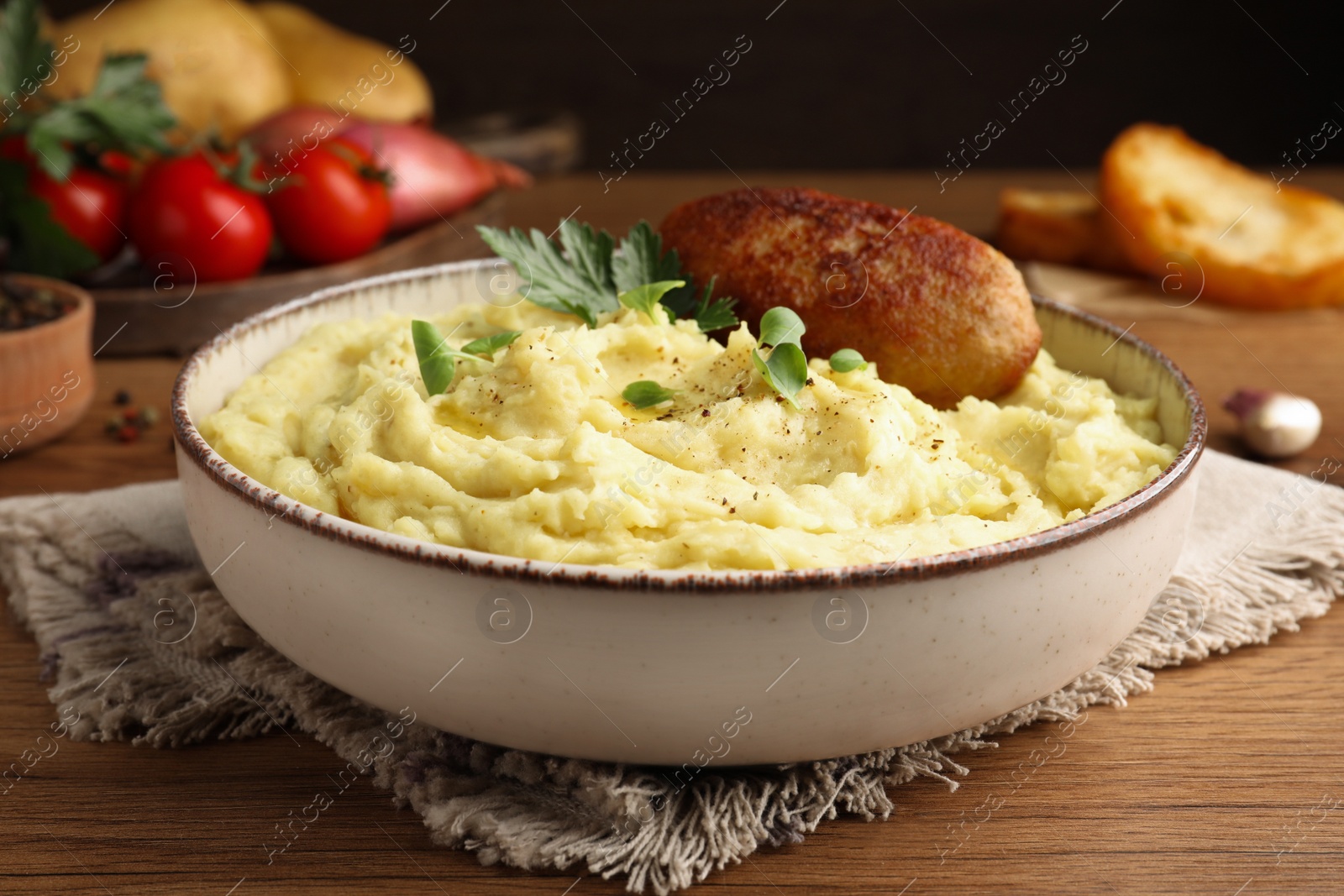 Photo of Bowl of tasty mashed potatoes with parsley, black pepper and cutlet served on wooden table, closeup