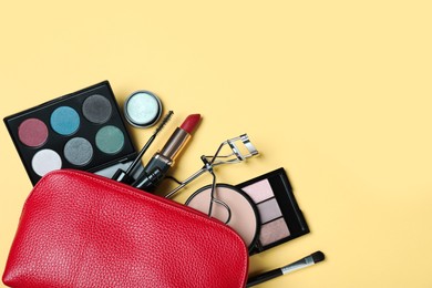 Cosmetic bag with makeup products and accessories on yellow background, flat lay. Space for text