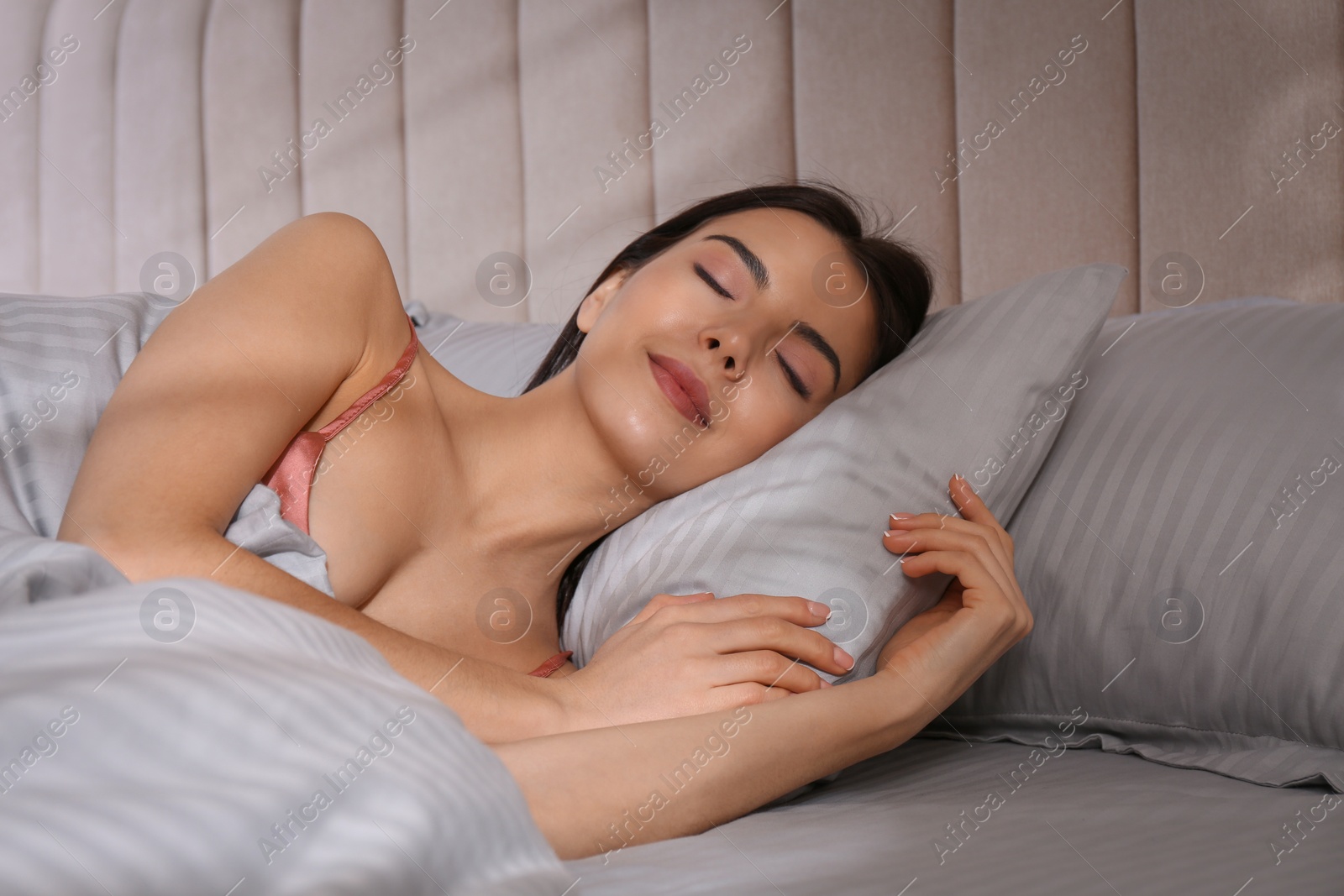 Photo of Woman sleeping in comfortable bed with light grey striped linens