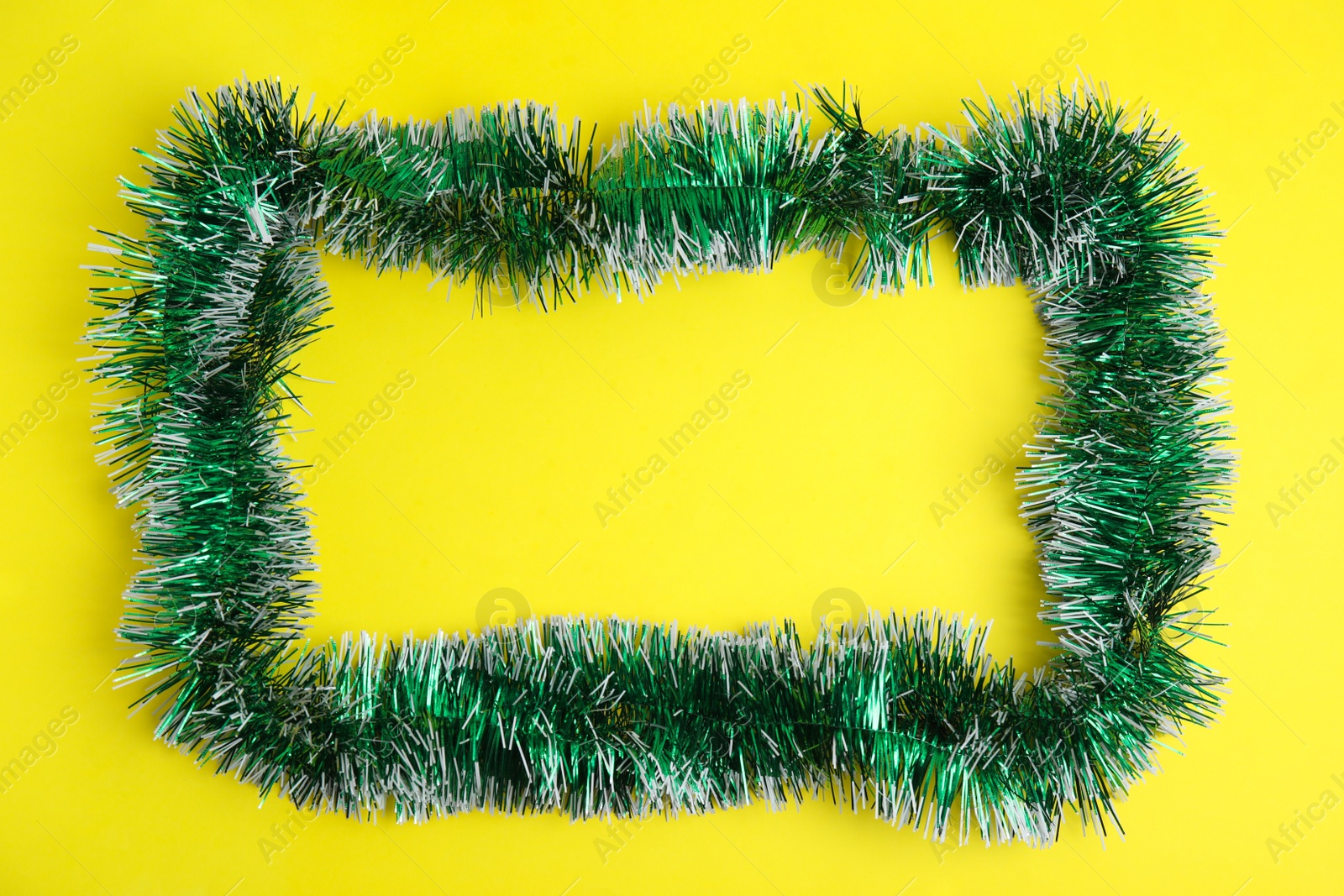 Photo of Frame of green tinsel on yellow background, top view. Space for text