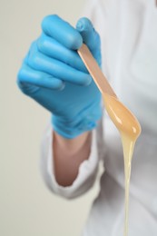 Photo of Woman in gloves holding spatula with hot depilatory wax, closeup