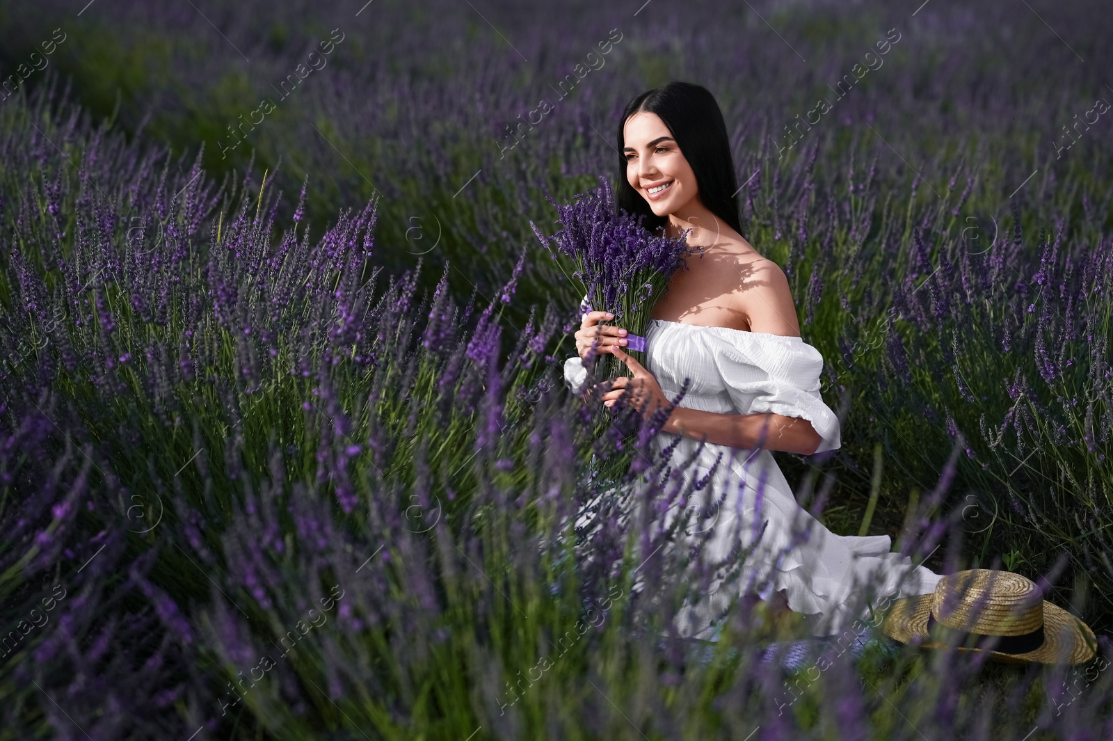 Photo of Beautiful young woman with bouquet sitting in lavender field