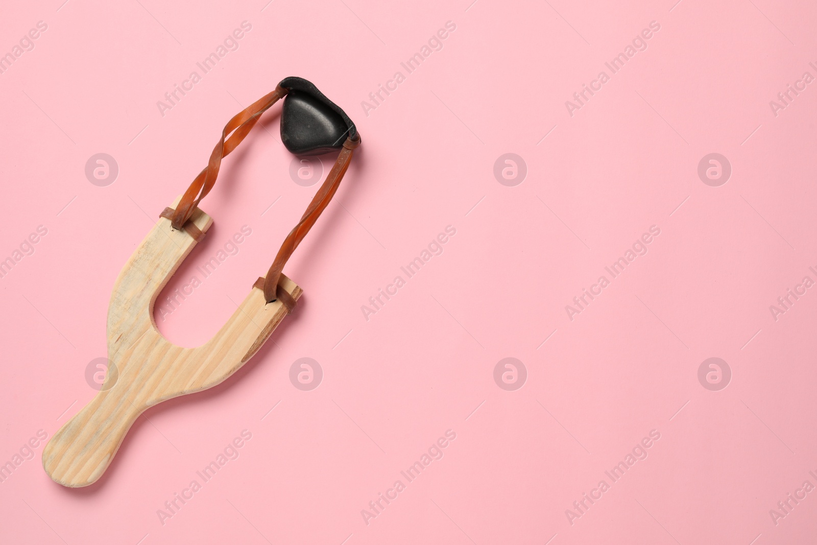 Photo of Wooden slingshot with pebble on pink background, top view. Space for text