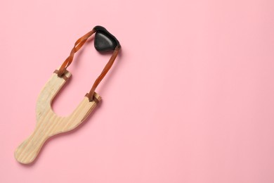 Wooden slingshot with pebble on pink background, top view. Space for text