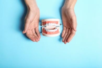Photo of Woman holding hands near educational model of oral cavity with teeth on color background, top view. Space for text