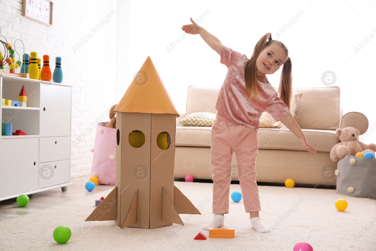 Photo of Cute little child playing with cardboard rocket at home