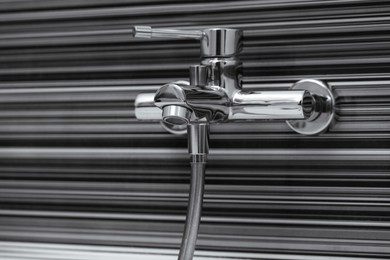 Shiny bath water tap installed on black and white wall