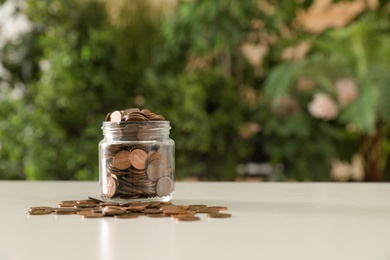 Photo of Donation jar with coins on table against blurred background. Space for text