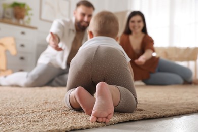 Happy parents watching their baby crawl on floor at home