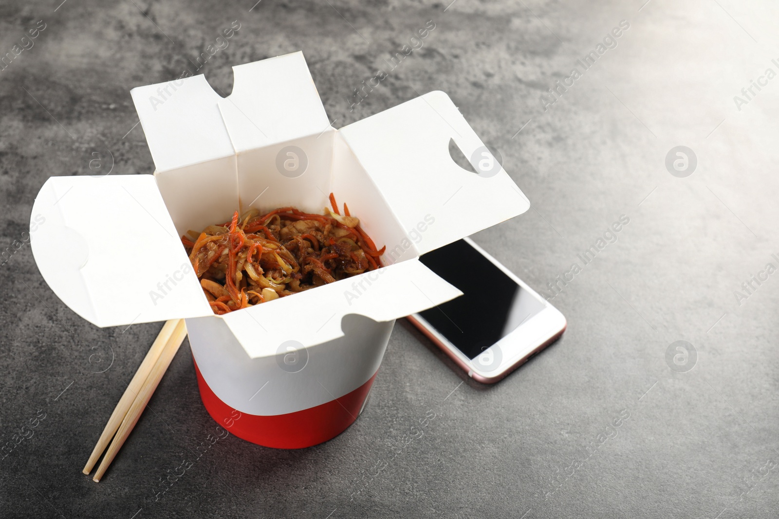 Photo of Smartphone and Chinese noodles on grey table. Food delivery