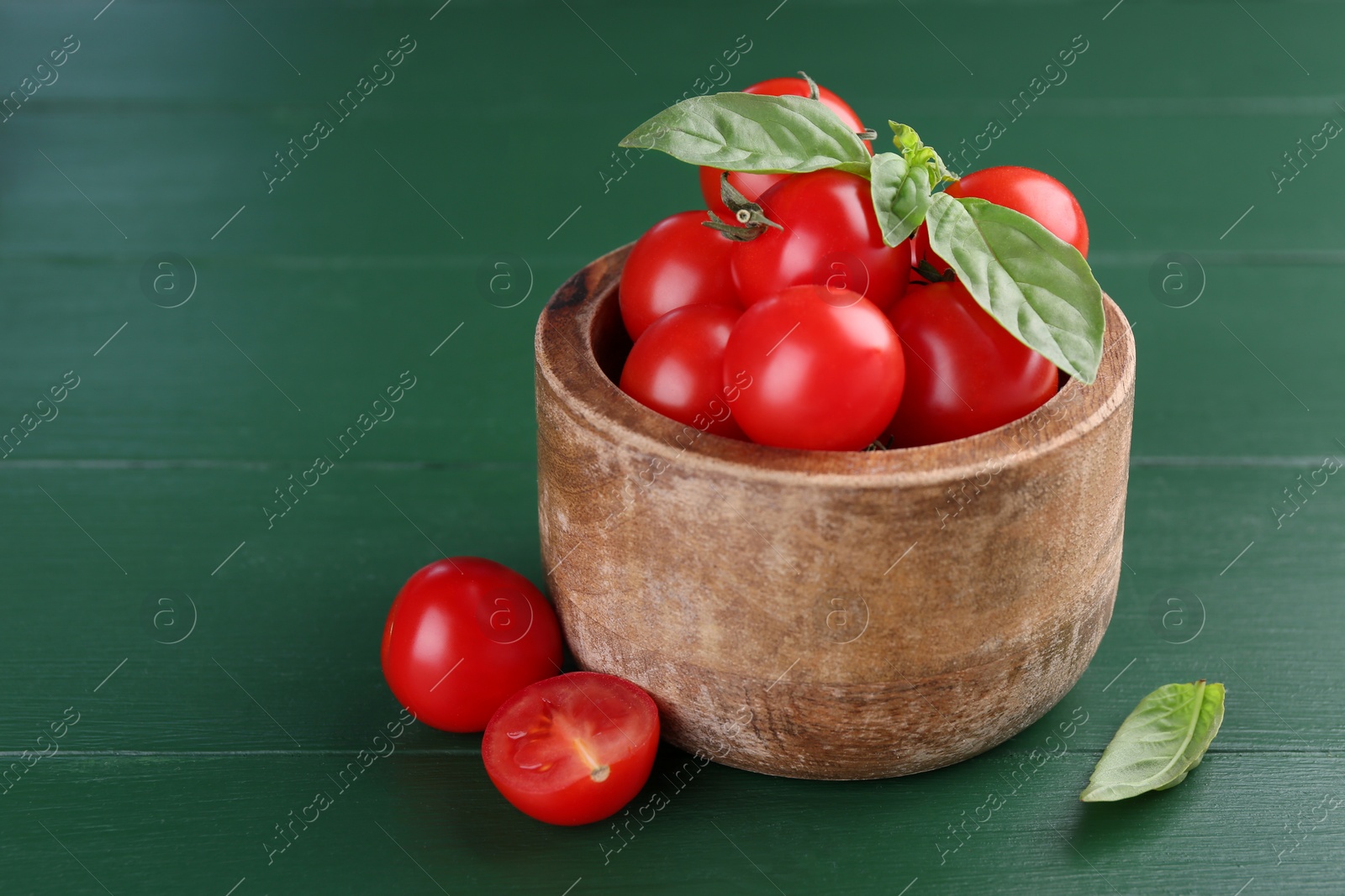 Photo of Ripe tomatoes in bowl on green wooden table, closeup. Space for text